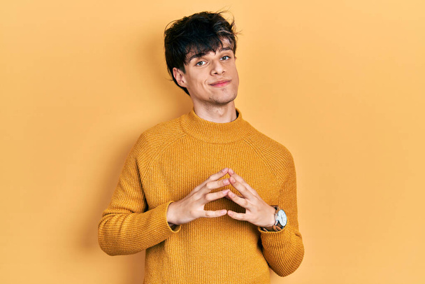 Hombre joven hipster guapo con manos suéter amarillo casual juntos y los dedos cruzados sonriendo relajado y alegre. éxito y optimismo  - Foto, Imagen