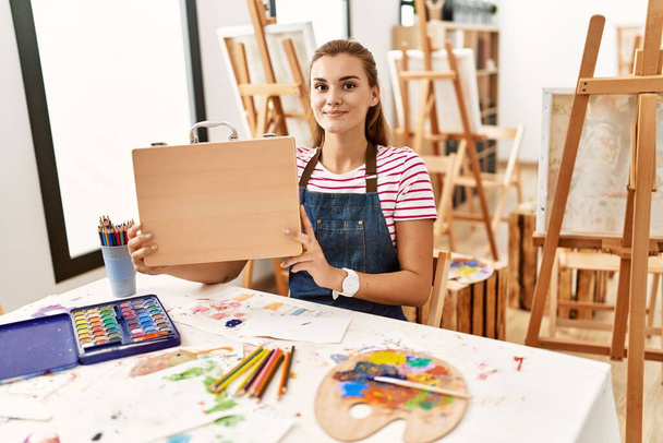 Jeune femme assise sur une table tenant une valise de dessin au studio d'art - Photo, image