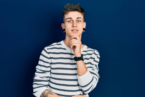 Young caucasian boy with ears dilation wearing casual striped shirt looking confident at the camera with smile with crossed arms and hand raised on chin. thinking positive.  - 写真・画像