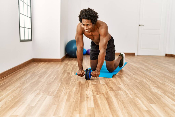 Young african american man training abs using roller at gym - 写真・画像
