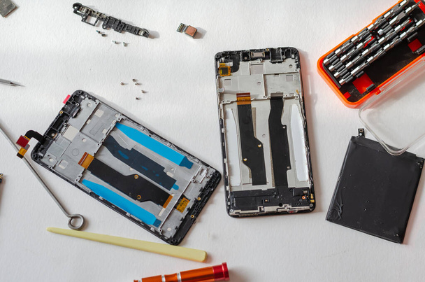Repair of smartphones concept. Hand tool and disassembled phone lying on the table. Part of a series. Indoors. Selective focus. - Foto, Bild