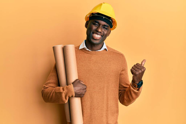 Young african american man wearing safety helmet holding blueprints screaming proud, celebrating victory and success very excited with raised arm  - Foto, imagen
