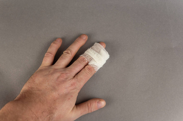 La mano de un hombre maduro con dedos índice vendados. El hombre sostiene su palma contra el fondo gris. Salud y Medicina. - Foto, imagen