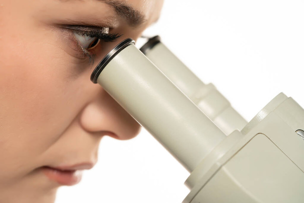 Macro Close Up Shot of a Female Scientist Looking into the Microscope. Vista lateral sobre un fondo blanco - Foto, imagen
