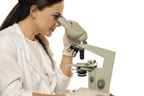 Female scientist looking through a microscope, white background. Side view - Foto, Bild