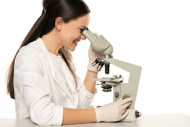 Щаслива жінка-вчена, яка дивиться через мікроскоп, білий фон
 - Фото, зображення
