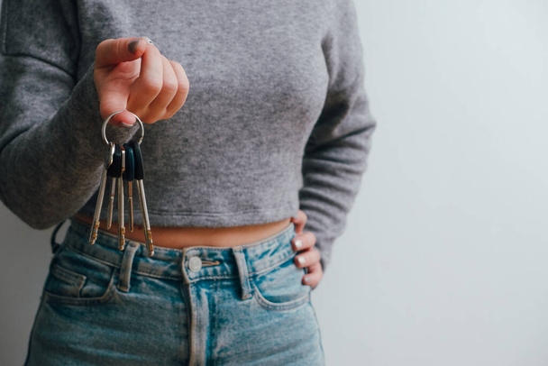 An attractive woman in jeans and a top holds out a bunch of keys in her hand. People lifestyle concept. copy space. Hold house bunch of keys, pointing index finger aside. - Valokuva, kuva
