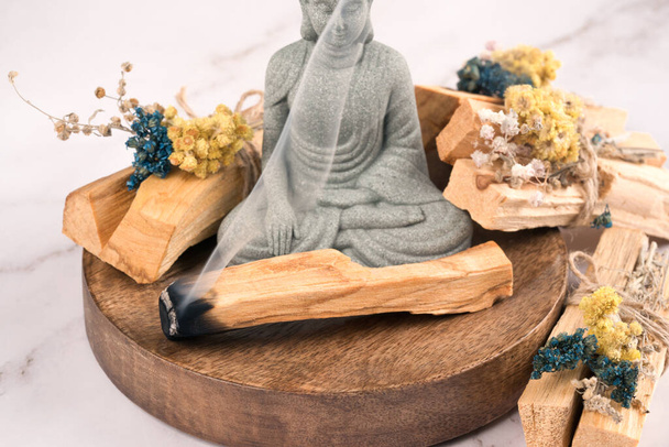 Holy wood sticks with dried flowers bouquet for meditation and spiritual  practices, wooden tray with palo santo sticks on white marble table  background, Stock image