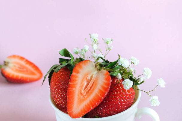 Zralé jahody v bílém hrnku, zblízka s květinami na růžovém pozadí. Selektivní soustředění. kopírovat prostor shora - Fotografie, Obrázek