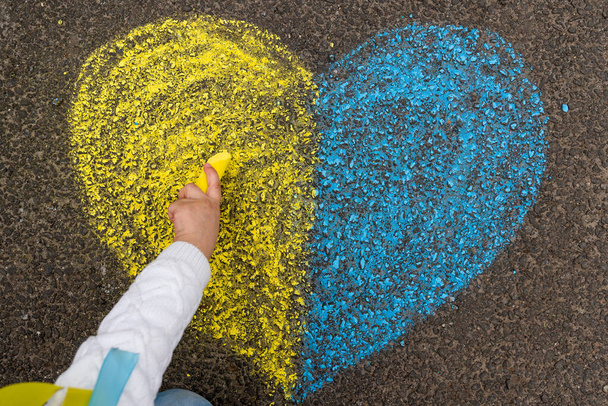 La main d'un enfant dessine un cœur avec des crayons sur le trottoir avec les couleurs patriotiques nationales ukrainiennes de jaune et de bleu. Arrêtez la guerre en Ukraine. Photo de haute qualité - Photo, image