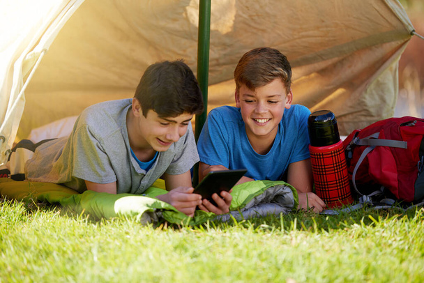 They brought some entertainment along. A young boy showing his friend something on a digital tablet while theyre camping. - Photo, Image