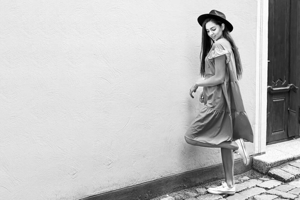mladá elegantní žena v šatech a klobouku na dlážděné staré městské ulici, černobílá - Fotografie, Obrázek