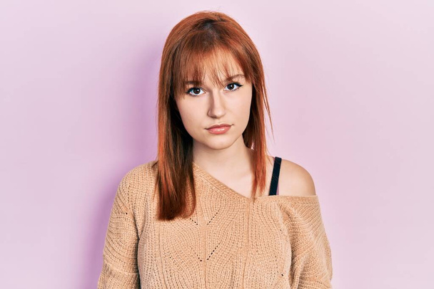 Vörös hajú fiatal nő alkalmi téli pulóvert visel komoly arckifejezéssel. egyszerű és természetes nézi a kamerát.  - Fotó, kép