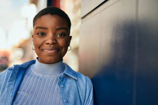 Genç Afrikalı Amerikalı kadın gülümseyerek şehirde mutlu mesut duruyor.. - Fotoğraf, Görsel