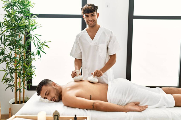 İki İspanyol fizyoterapist ve hasta masaj yapıyor. Güzellik merkezinde Tayland çantaları kullanıyorlar. - Fotoğraf, Görsel
