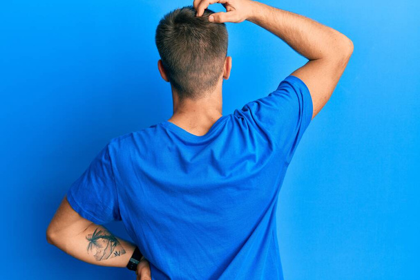 Mladý kavkazský muž v neformální modré tričko pozpátku přemýšlí o pochybách s rukou na hlavě  - Fotografie, Obrázek