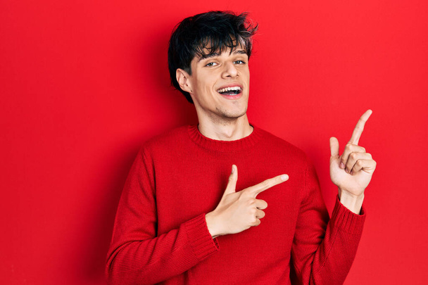 Handsome hipster young man wearing red winter sweater smiling and looking at the camera pointing with two hands and fingers to the side.  - Photo, Image