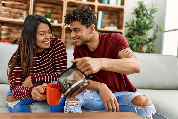 Giovane coppia latina sorridente felice bere caffè seduto sul divano a casa. - Foto, immagini