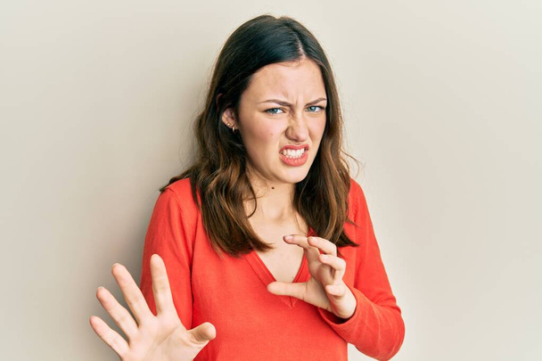 Young brunette woman wearing casual clothes disgusted expression, displeased and fearful doing disgust face because aversion reaction. with hands raised  - Photo, Image