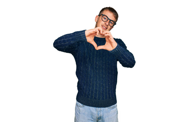 Young blond man wearing casual clothes and glasses smiling in love doing heart symbol shape with hands. romantic concept.  - Photo, Image