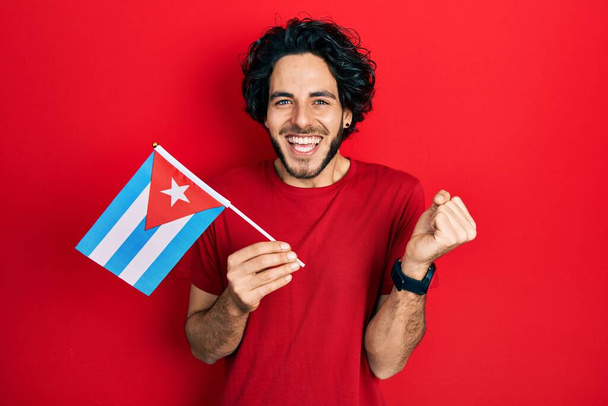 キューバ国旗を掲揚するハンサムなヒスパニック系の男は誇りに思って叫んで勝利と成功を祝う非常に腕を上げ興奮して  - 写真・画像