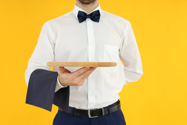 Waiter man holds empty tray on yellow background - Φωτογραφία, εικόνα
