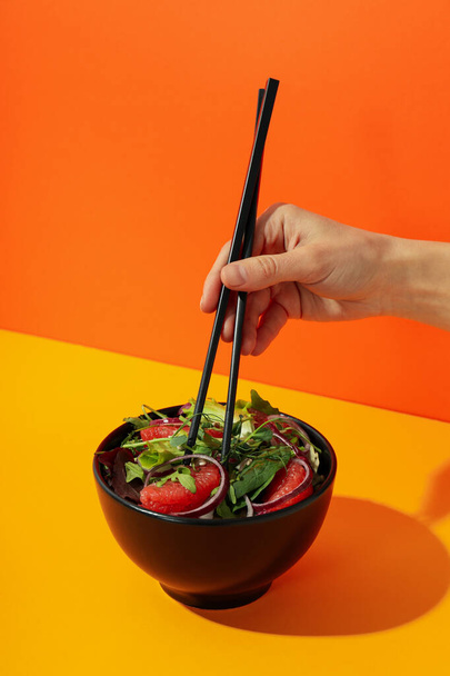 Çubuklu kadın eli ve kırmızı turuncu salata. - Fotoğraf, Görsel