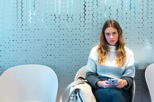 Молода жінка використовує мобільний телефон під час очікування зустрічі з лікарями в залі очікування
. - Фото, зображення