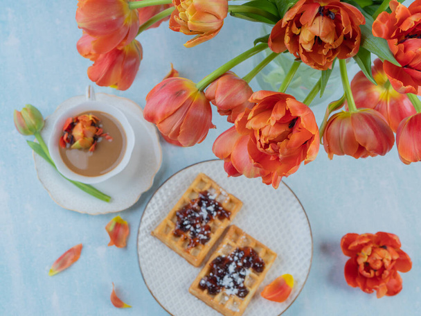 Scarlet, red tulips in a vase and a white cup with coffee and French waffles. The concept of congratulations and old holidays. There is a place for text. - Zdjęcie, obraz