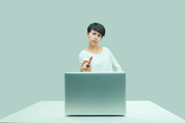 Wściekła, zwyczajna młoda kobieta gestykuluje w stronę ekranu laptopa, wznosi środkowy palec w kierunku tego, z czym się nie zgadza: niesprawiedliwości, zła - Zdjęcie, obraz