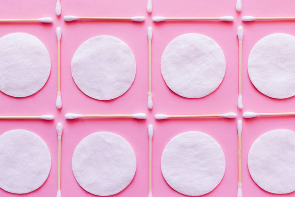 flat lay of white cotton pads and ear sticks on pink background, top view - Foto, afbeelding