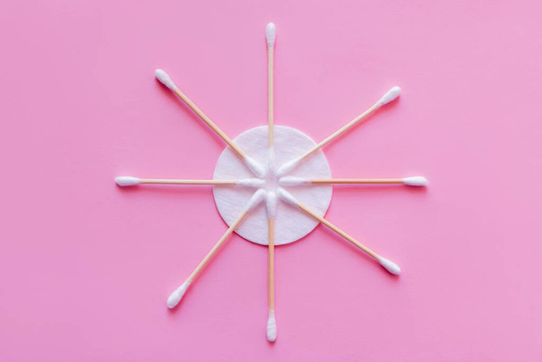 плоский шар косметичних вушних паличок біля білої бавовняної прокладки на рожевому фоні, вид зверху
 - Фото, зображення