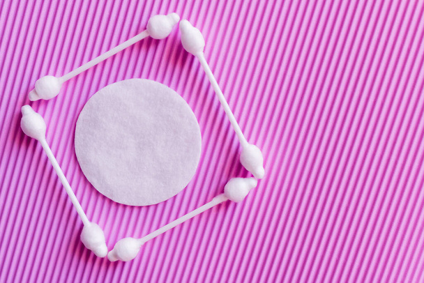 top view of white cotton pad in frame of ear sticks on purple textured background - 写真・画像
