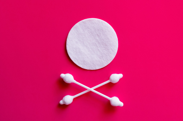 crossed ear sticks under white cotton pad on pink background, top view - Foto, Imagen