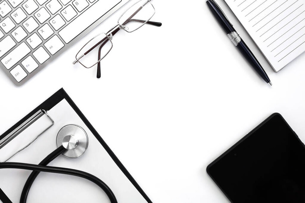 Medical stethoscope, keyboard, notebook with pen and black tablet on white background. Doctor's workplace. Top view. Flatlay composition. Medical concept. - Photo, Image