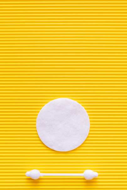 top view of white cotton pad and ear stick on yellow textured background - Φωτογραφία, εικόνα