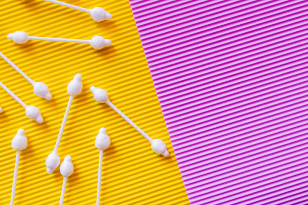 вид зверху на гігієнічні вушні палички на жовтому та фіолетовому текстурованому фоні
 - Фото, зображення