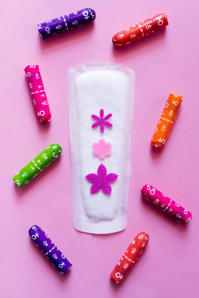 top view of panty liner with decorative flowers near packed tampons on violet background - Fotó, kép