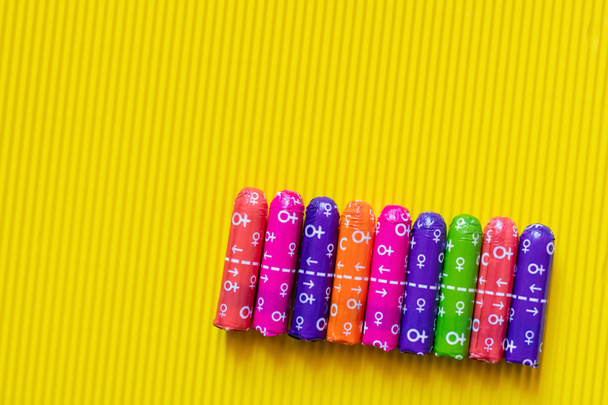 top view of tampons in multicolored packing with female signs on yellow textured background - Фото, изображение