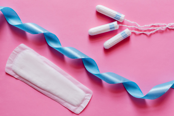 top view of tampons and soft panty liner near blue satin ribbon on pink background - Foto, Bild