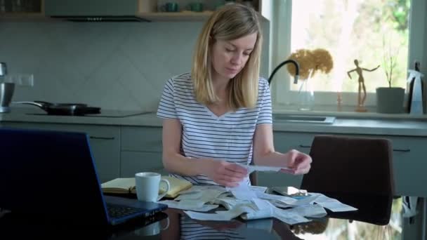 Znepokojená žena při pohledu na papírové účty a počítání výdajů, domácí rozpočet - Záběry, video