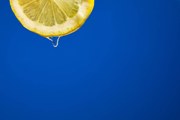 Tranche fraîche de jus de citron goutte à goutte sur fond bleu, goutte à goutte d'agrumes isolé, espace de copie. - Photo, image