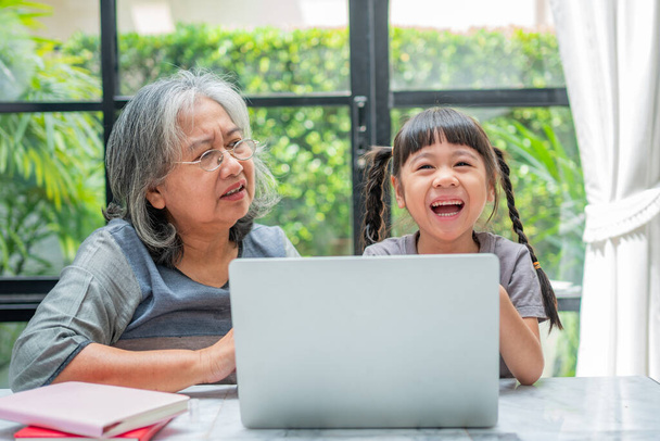 Азійська бабуся з двома онуками бавляться і грають в освітні ігри онлайн з комп'ютерним записником вдома у вітальні. Концепція онлайн освіти і турботи батьків.. - Фото, зображення