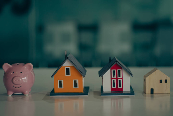 Модель нескольких небольших домов и копилок на столе, размытый фон. Экономия денег Идеи для домашних названий - Фото, изображение