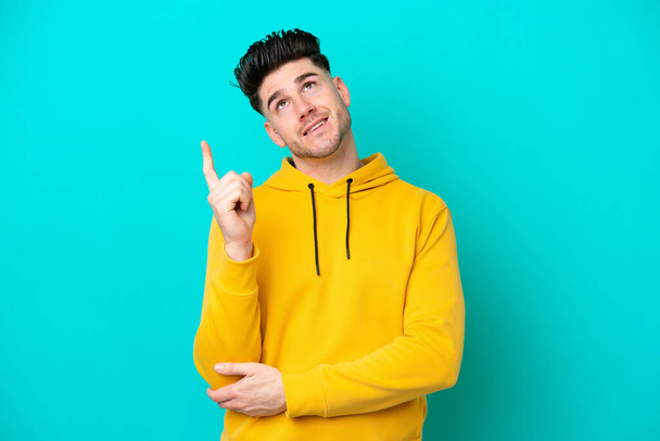 Young caucasian man isolated on blue background pointing up a great idea - Photo, Image