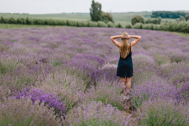 Beautiful girl in dress stand on purple the lavender field. Beautiful woman walk and look on the lavender field on sunset in France. Soft focus. Enjoy on the floral glade, summer nature. Back view. - Fotoğraf, Görsel