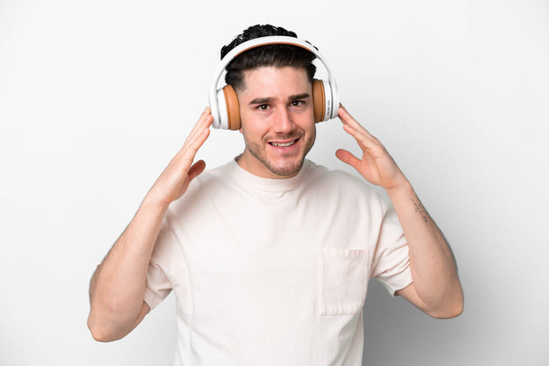 Young caucasian man isolated on white background listening music - 写真・画像