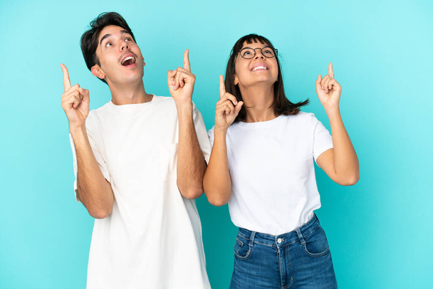 Молодая пара смешанной расы изолированы на синем фоне указывая указательным пальцем отличная идея - Фото, изображение