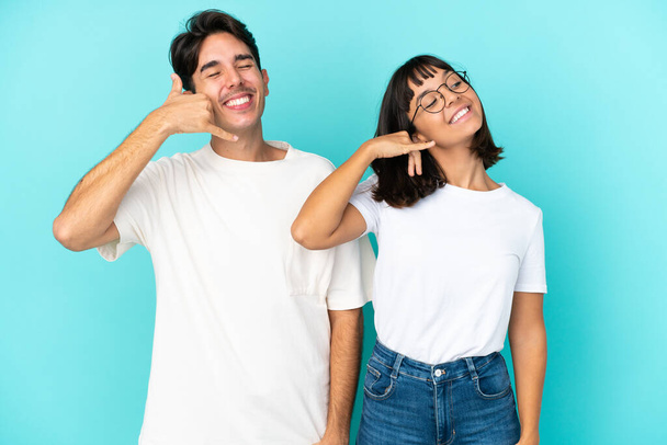 Young mixed race couple isolated on blue background making phone gesture. Call me back sign - Photo, Image