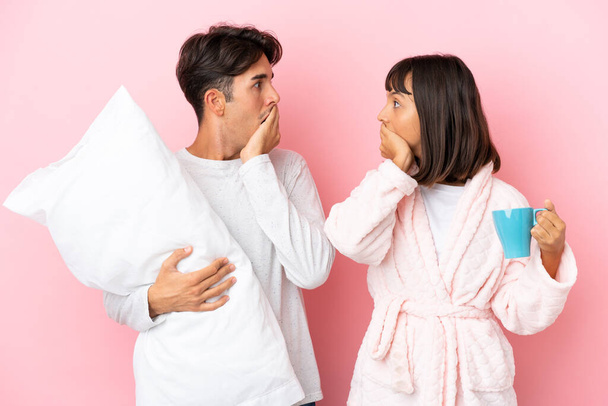 Junges Paar im Pyjama isoliert auf rosa Hintergrund bedeckt Mund mit Händen für etwas Unangemessenes sagen - Foto, Bild